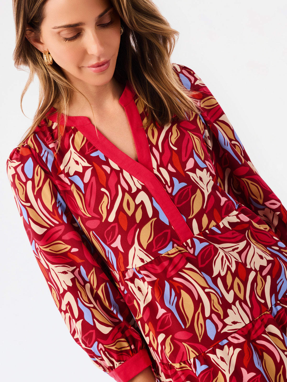 A woman wearing a long-sleeve red dress with a bold abstract floral pattern in beige, brown, and light blue, photographed against a clean white background.
