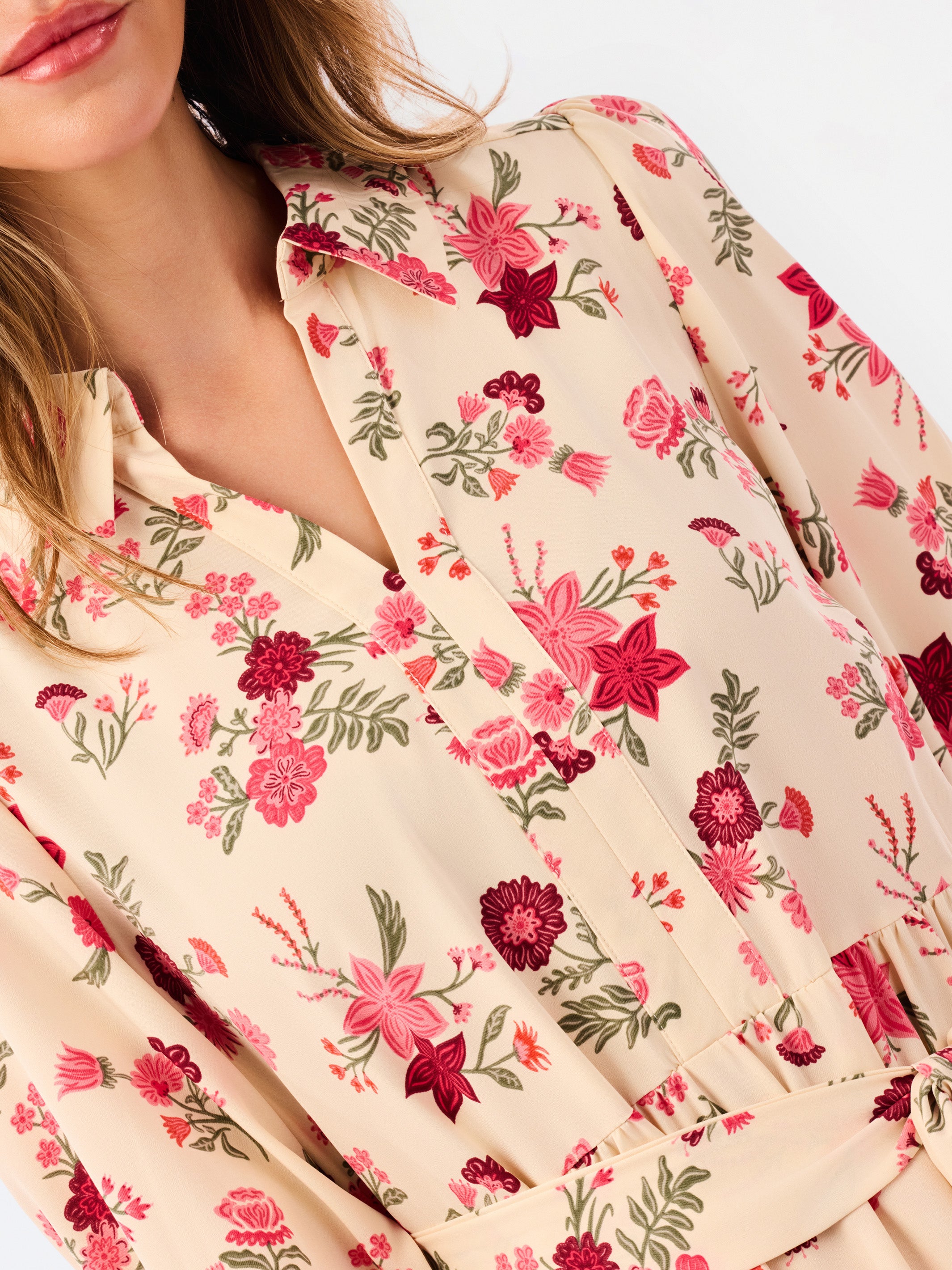 A close-up of a woman wearing a cream-colored long-sleeve blouse with a vibrant pink, red, and green floral pattern.