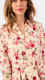 A woman wearing a cream-colored long-sleeve blouse with a vibrant red and pink floral print and green leaves, featuring a button-down front and a matching fabric tie belt at the waist.