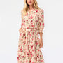 A woman modeling a beige midi shirt dress with a red and pink floral print, featuring a tie waist and 3/4 sleeves, set against a plain white studio background.