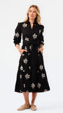 A woman modeling a black midi shirt dress with a beige floral print, standing against a plain white studio background.