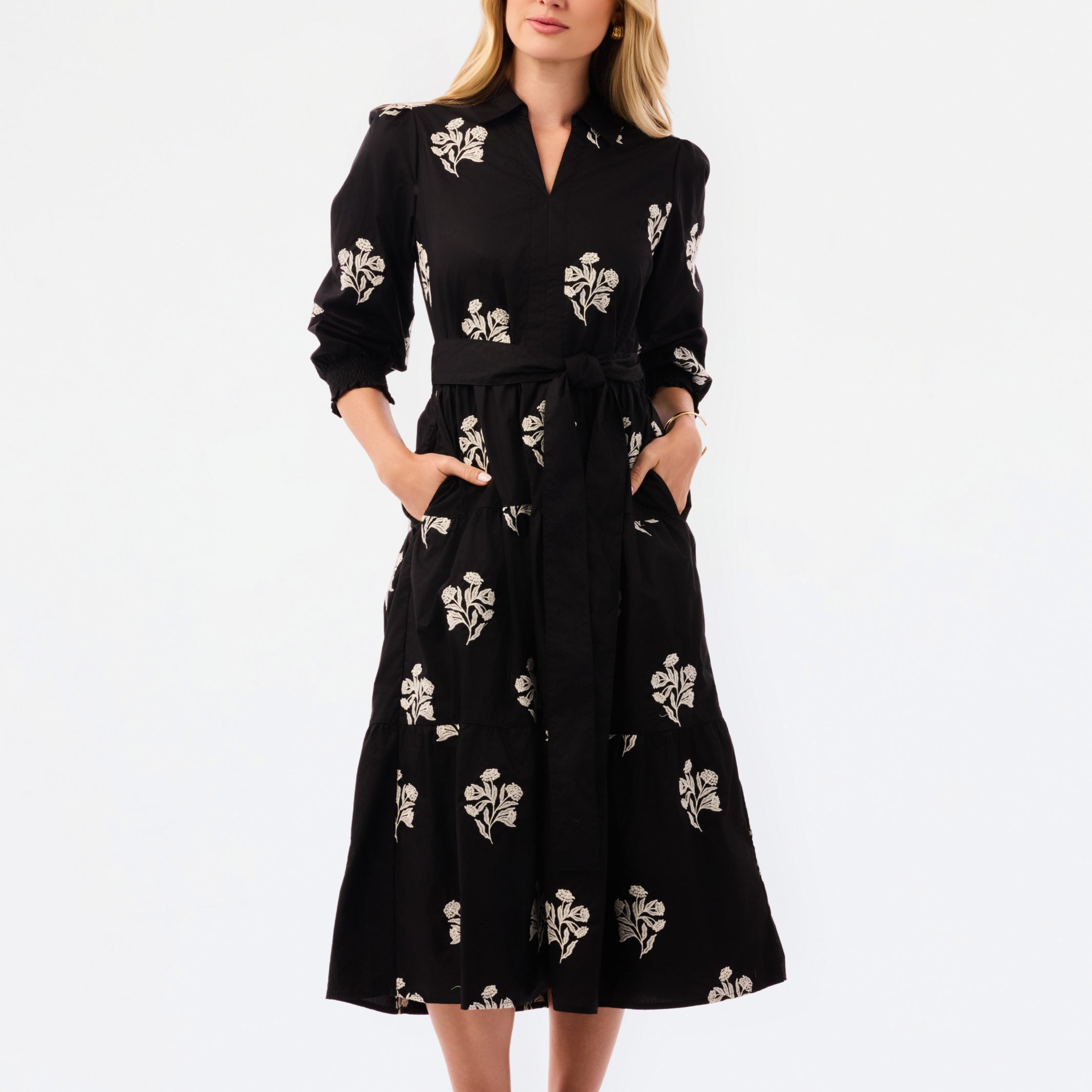A woman modeling a black midi shirt dress with a beige floral print, standing against a plain white studio background.