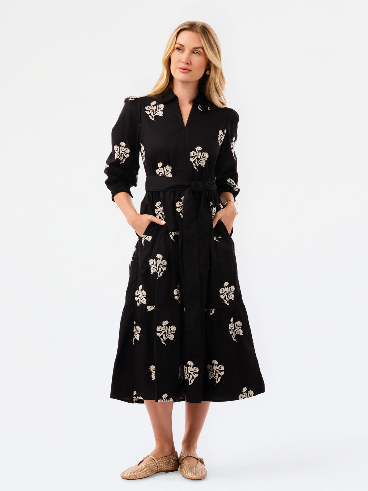 A woman modeling a black midi shirt dress with a beige floral print, standing against a plain white studio background.