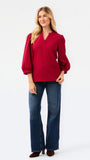 A woman wearing a red long-sleeve blouse with puff sleeves and a split neckline, paired with blue jeans, photographed against a plain white studio background.