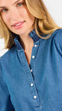 Blonde woman wearing a long sleeve denim shirt with navy blue trim and wearing creme pants