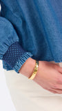 Blonde woman wearing a long sleeve denim shirt with navy blue trim and wearing creme pants