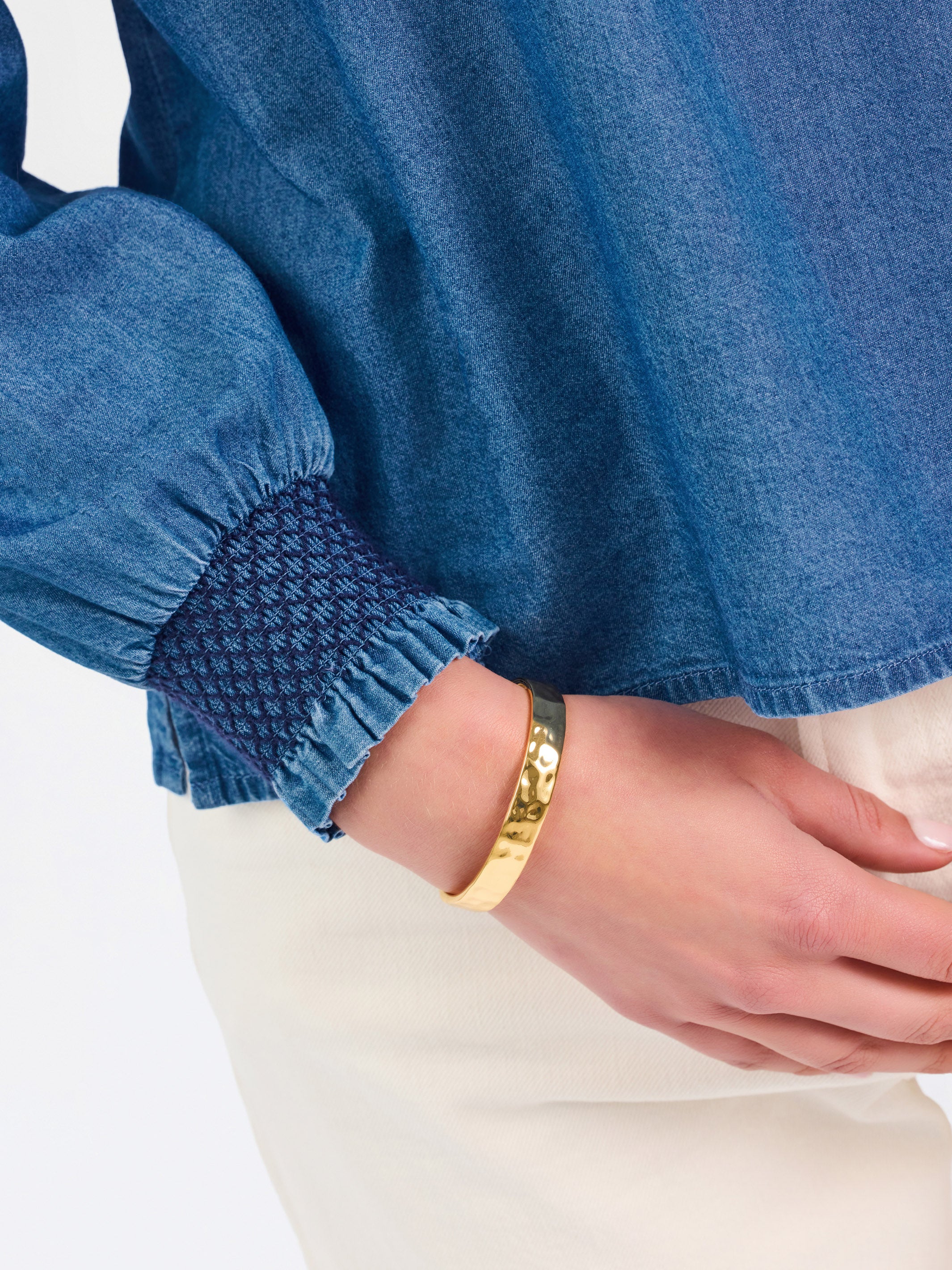 Blonde woman wearing a long sleeve denim shirt with navy blue trim and wearing creme pants