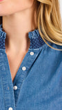 Blonde woman wearing a long sleeve denim shirt with navy blue trim and wearing creme pants
