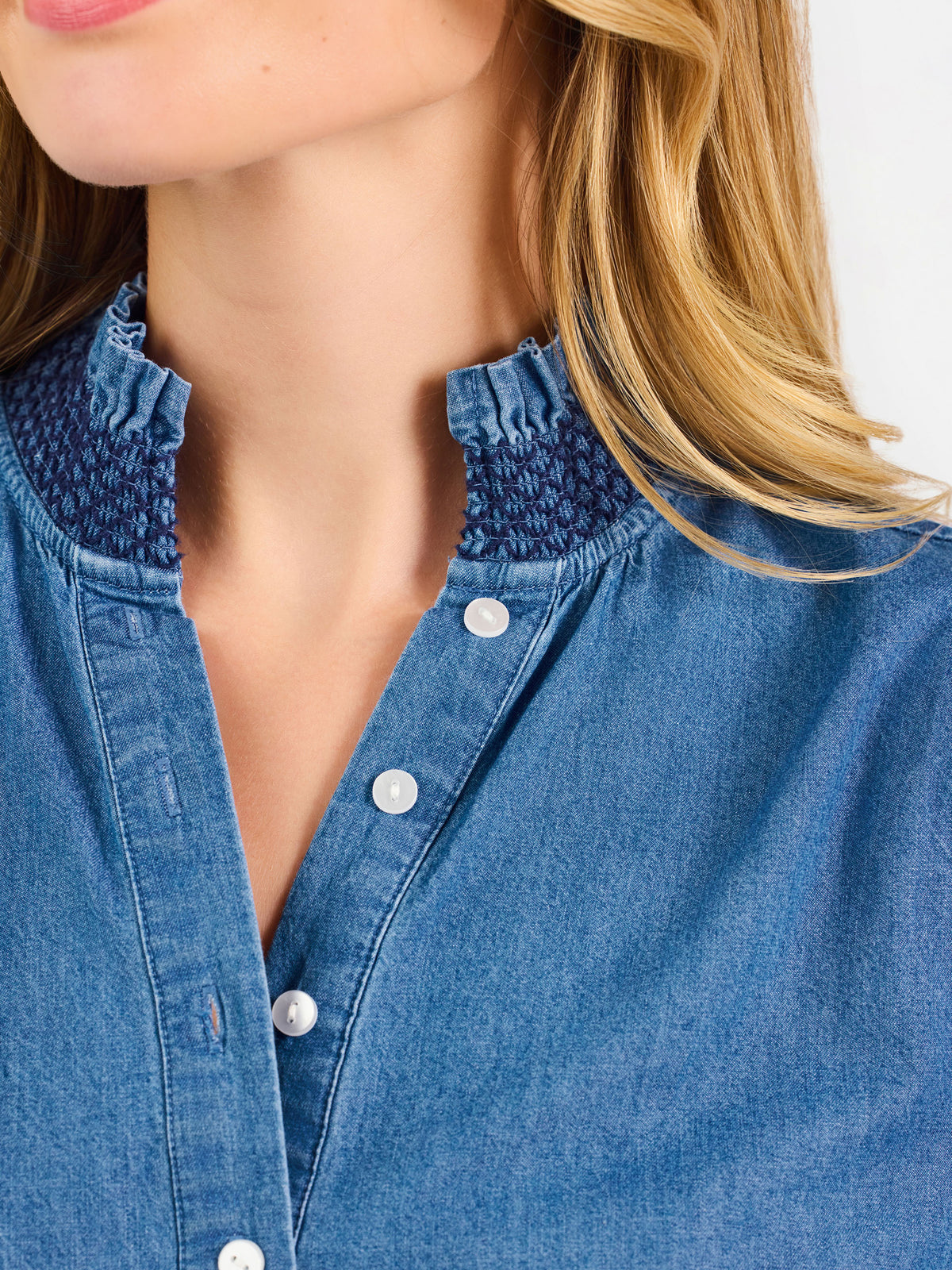Blonde woman wearing a long sleeve denim shirt with navy blue trim and wearing creme pants