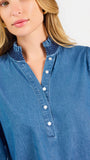 Blonde woman wearing a long sleeve denim shirt with navy blue trim and wearing creme pants