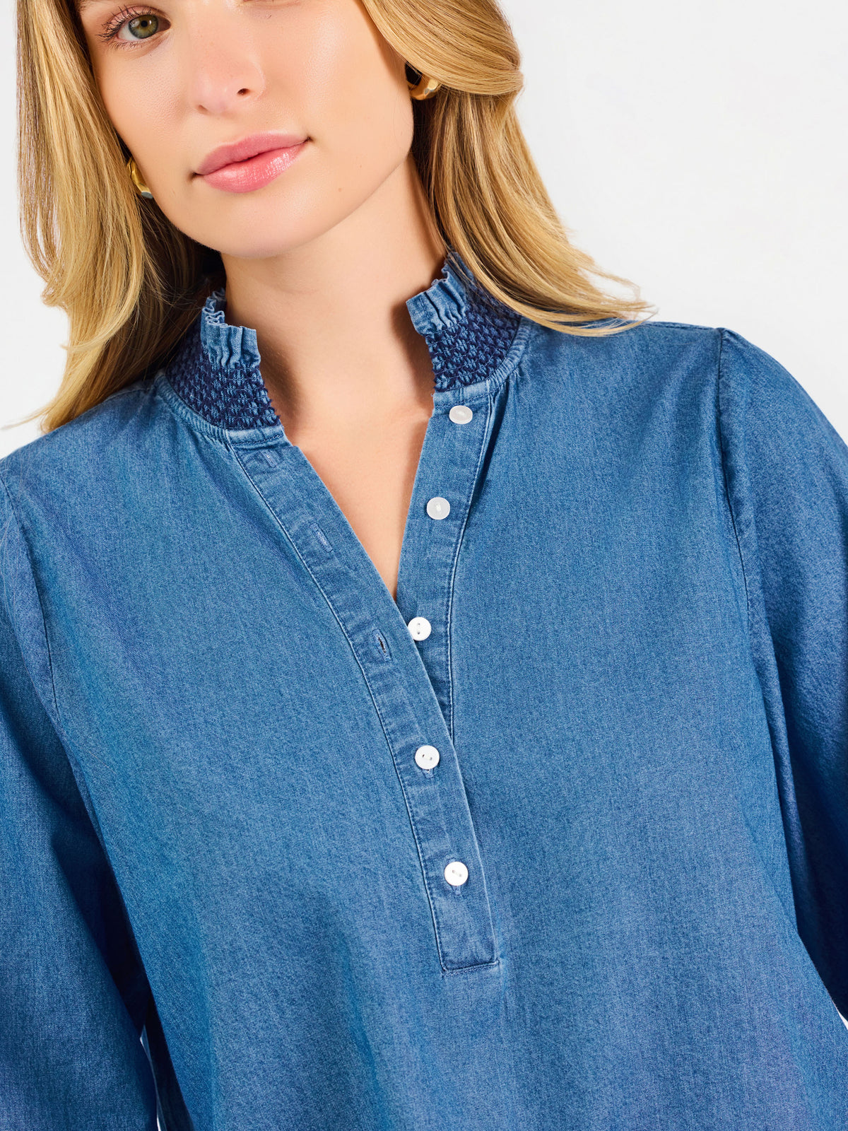 Blonde woman wearing a long sleeve denim shirt with navy blue trim and wearing creme pants