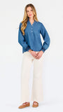 Blonde woman wearing a long sleeve denim shirt with navy blue trim and wearing creme pants