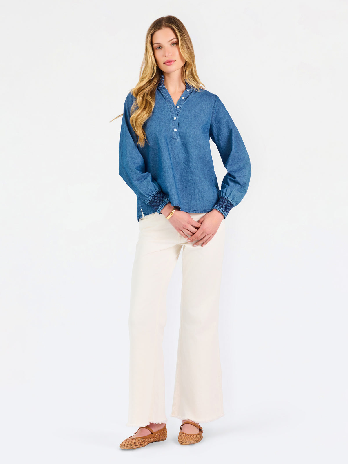Blonde woman wearing a long sleeve denim shirt with navy blue trim and wearing creme pants