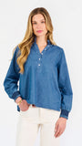 Blonde woman wearing a long sleeve denim shirt with navy blue trim and wearing creme pants