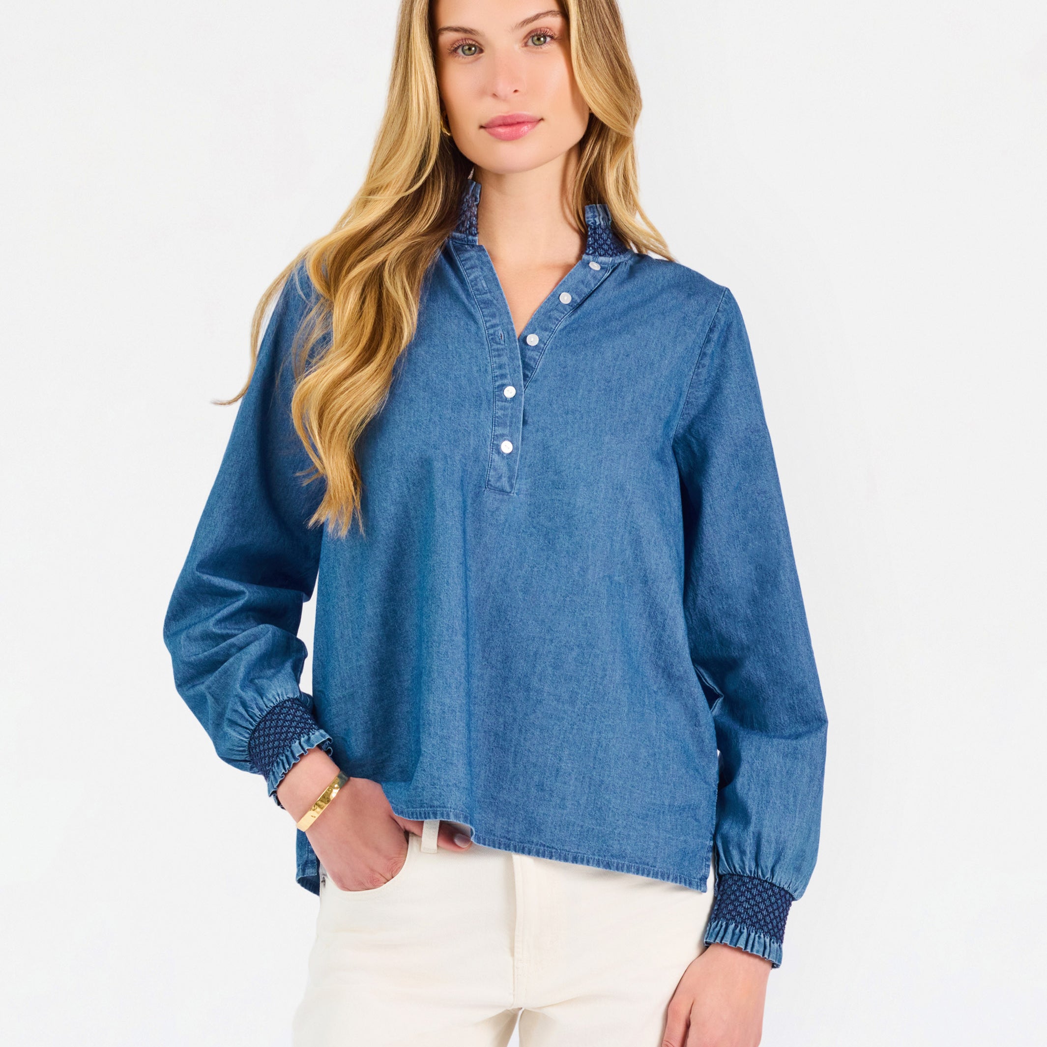 Blonde woman wearing a long sleeve denim shirt with navy blue trim and wearing creme pants