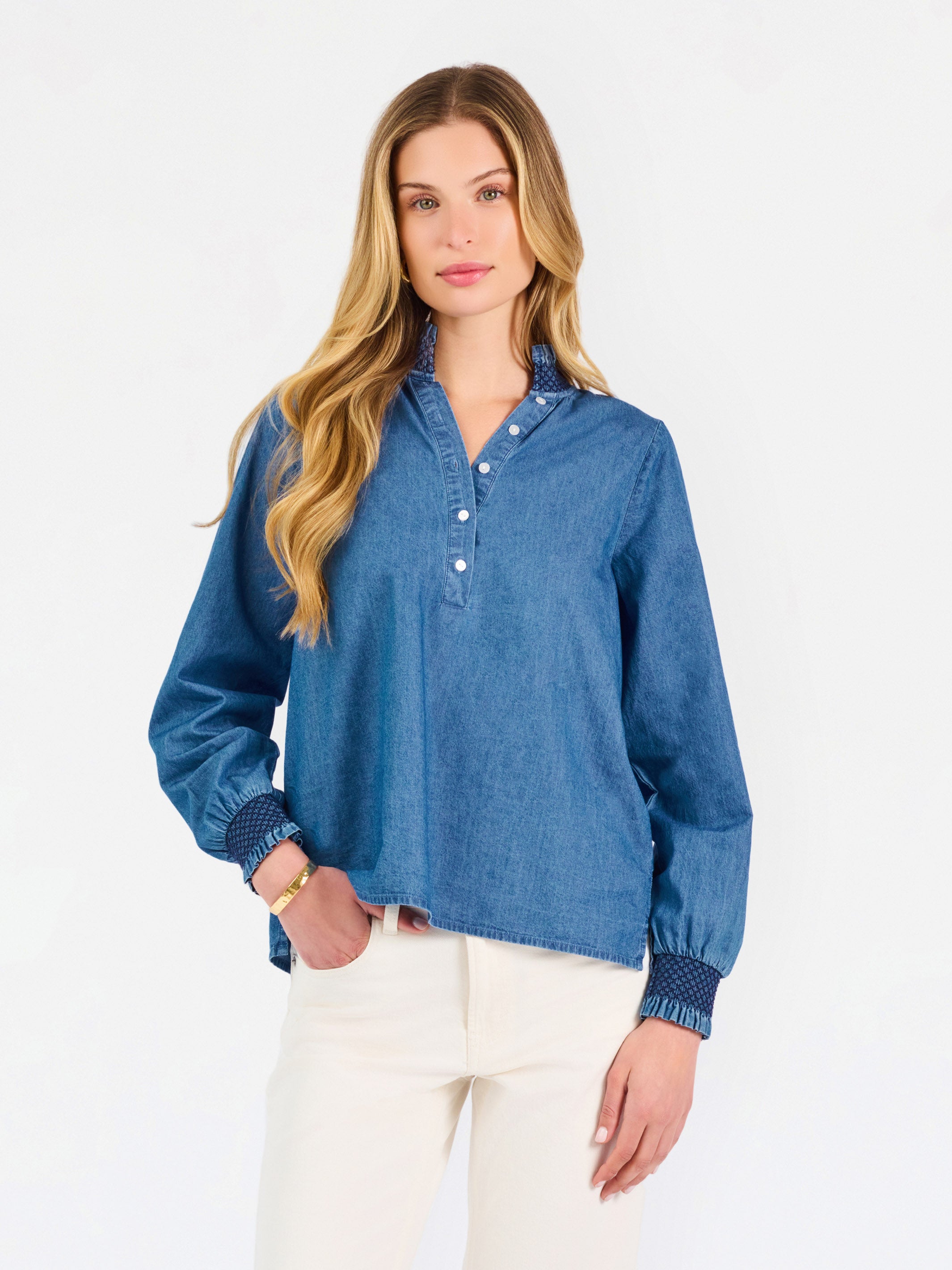 Blonde woman wearing a long sleeve denim shirt with navy blue trim and wearing creme pants