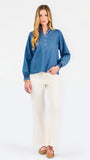 Blonde woman wearing a long sleeve denim shirt with navy blue trim and wearing creme pants