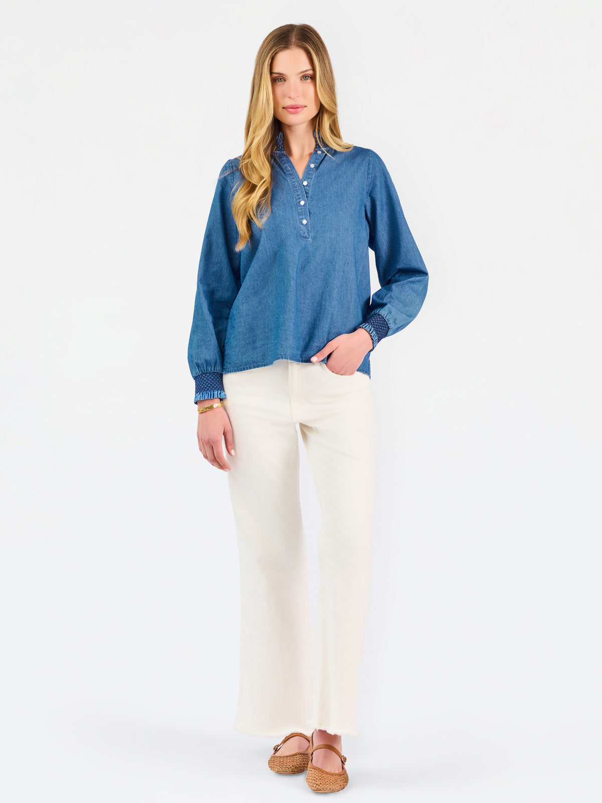 Blonde woman wearing a long sleeve denim shirt with navy blue trim and wearing creme pants