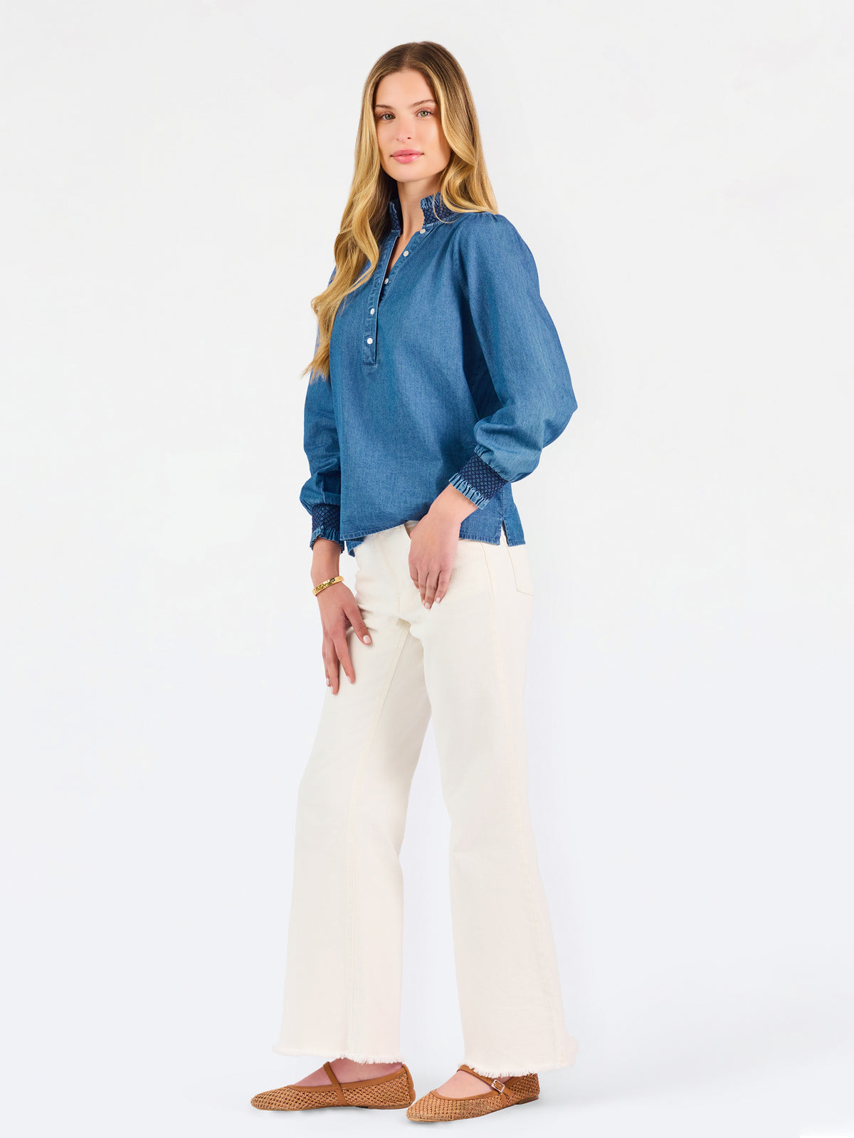 Blonde woman wearing a long sleeve denim shirt with navy blue trim and wearing creme pants