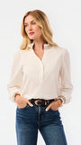 A blonde woman wearing a cream-colored long-sleeve blouse with lace trim at the collar and cuffs, paired with blue jeans, against a plain white studio background.