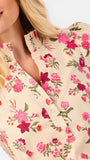 Close-up of a woman wearing a cream-colored blouse with a vibrant pink, red, and green floral print. The blouse features a ruffled high collar and a button-down front.
