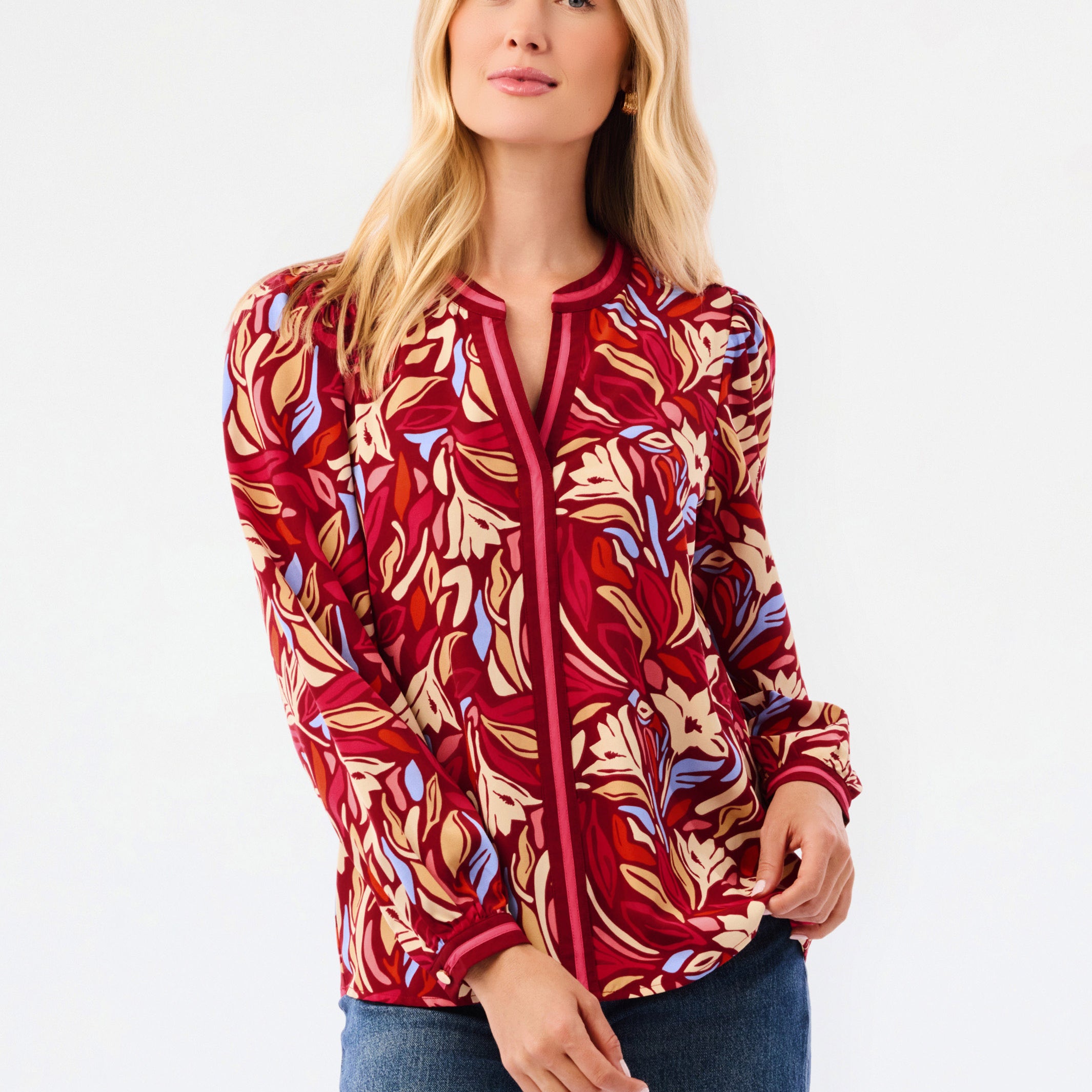 A woman modeling a red and beige abstract patterned top with blue jeans, photographed against a plain white studio background.