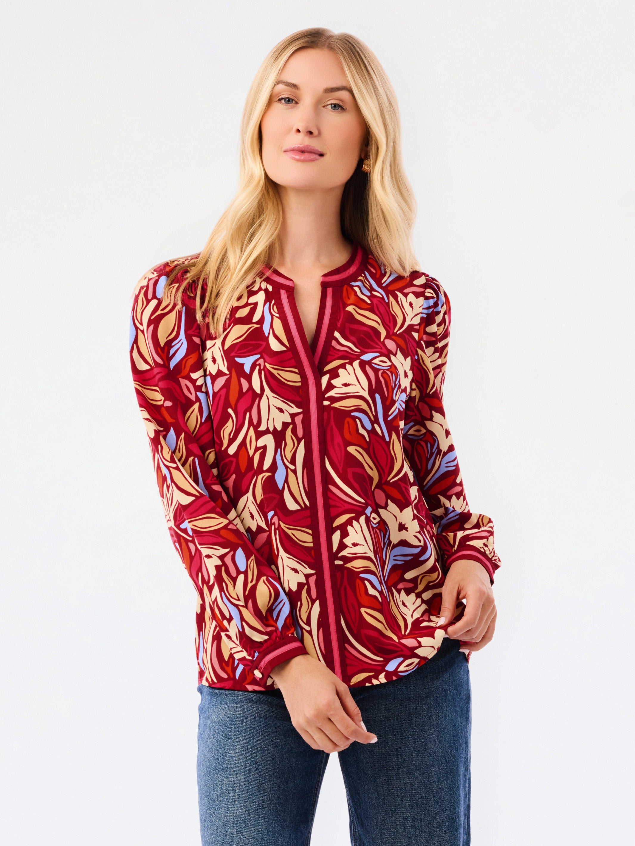 A woman modeling a red and beige abstract patterned top with blue jeans, photographed against a plain white studio background.
