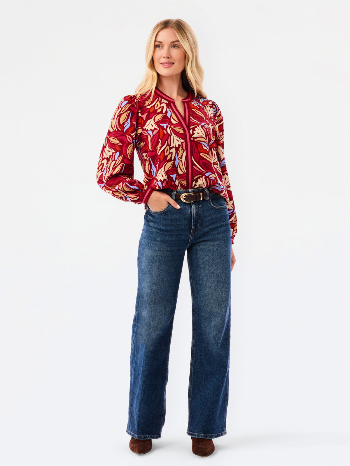 A woman modeling a red and beige abstract patterned top with blue jeans, photographed against a plain white studio background.