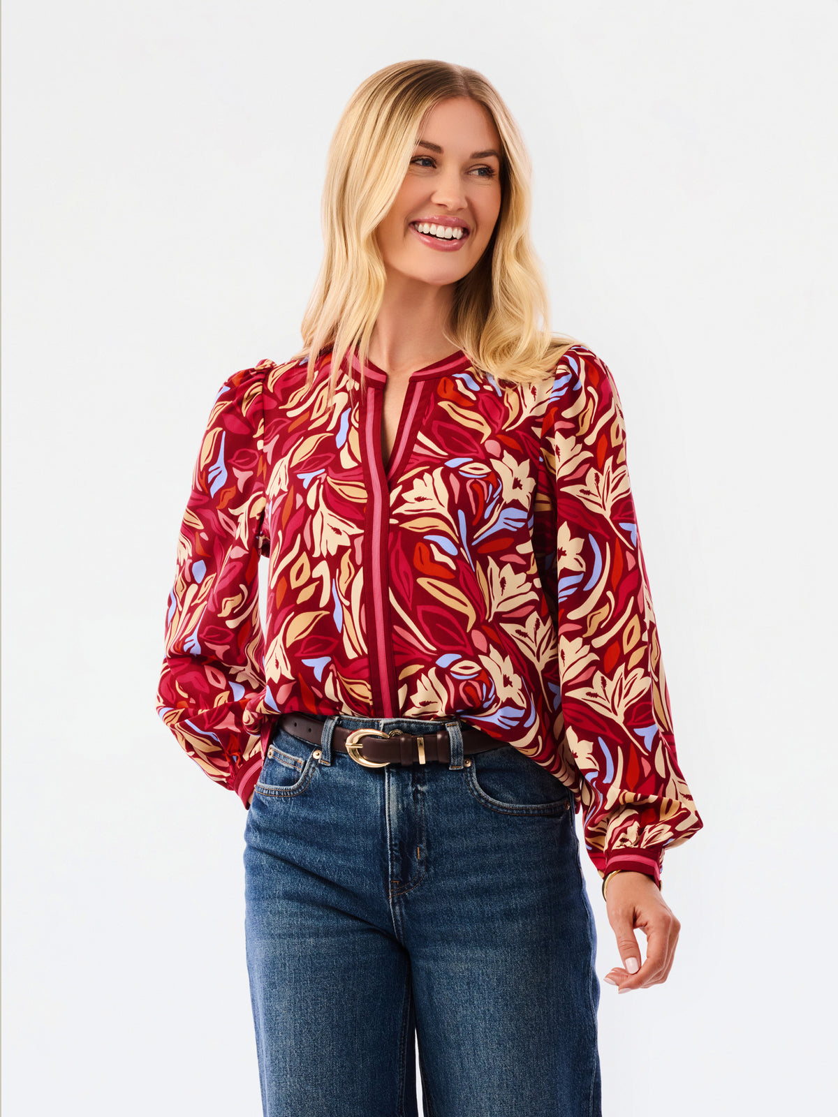 A woman modeling a red and beige abstract patterned top with blue jeans, photographed against a plain white studio background.