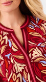 A woman modeling a red and beige abstract patterned top with blue jeans, photographed against a plain white studio background.