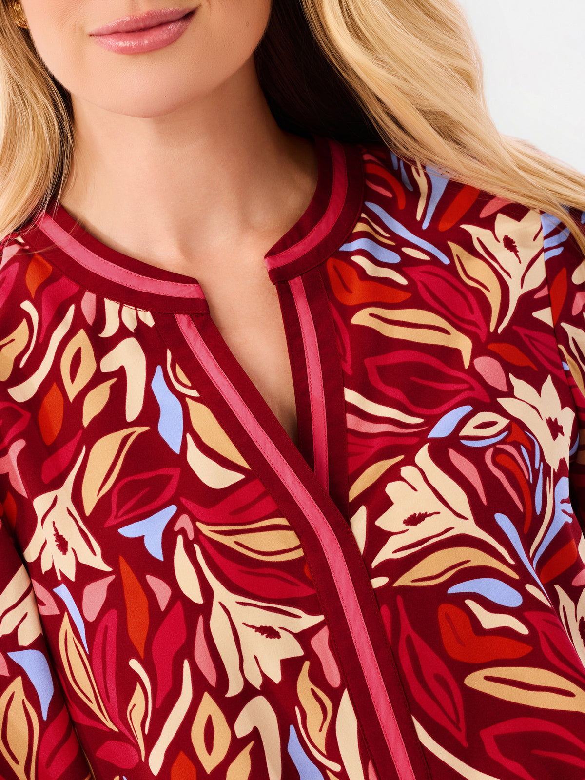 A woman modeling a red and beige abstract patterned top with blue jeans, photographed against a plain white studio background.