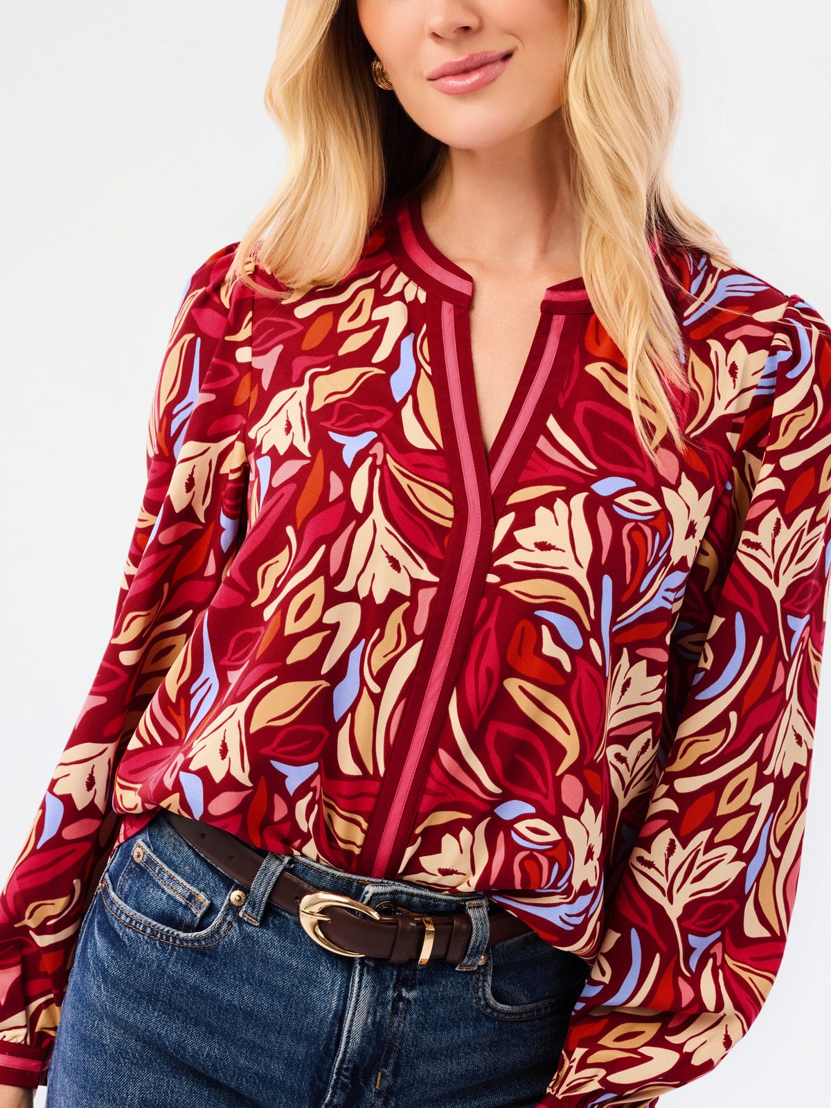 A woman modeling a red and beige abstract patterned top with blue jeans, photographed against a plain white studio background.