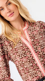A smiling blonde woman models a long-sleeve patterned blouse with pink trim and blue jeans against a plain white studio background.