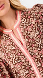 A smiling blonde woman models a long-sleeve patterned blouse with pink trim and blue jeans against a plain white studio background.