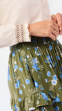 Close-up of a person wearing an olive green tiered skirt with a blue and white floral print, paired with a cream blouse featuring a lace cuff.