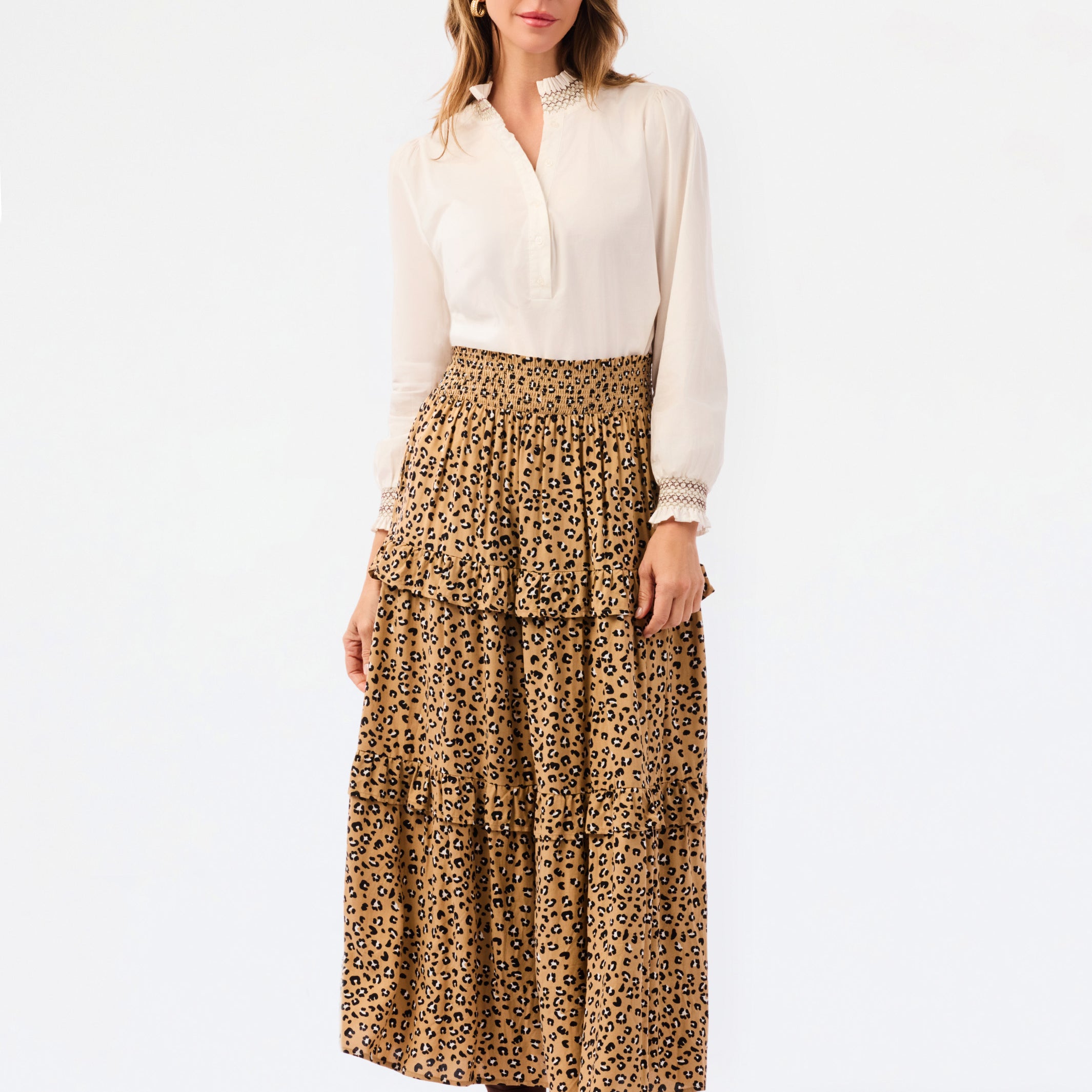 A woman modeling a white long-sleeve blouse and a tiered leopard-print maxi skirt, paired with dark brown ankle boots, against a plain white studio background.