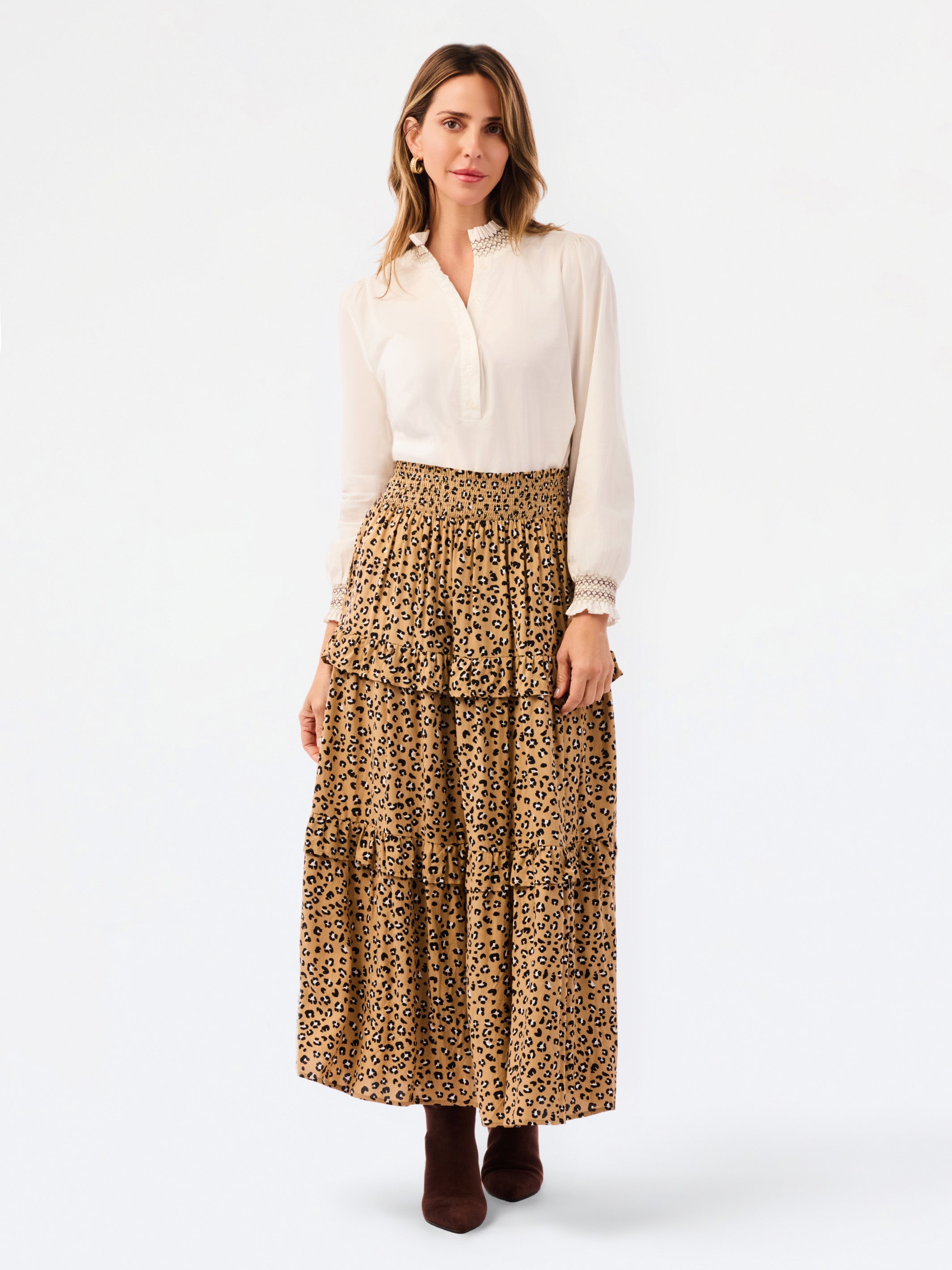 A woman modeling a white long-sleeve blouse and a tiered leopard-print maxi skirt, paired with dark brown ankle boots, against a plain white studio background.