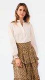 A woman modeling a white long-sleeve blouse with a lace-trimmed collar and cuffs, paired with a brown leopard-print tiered skirt, against a plain white background.