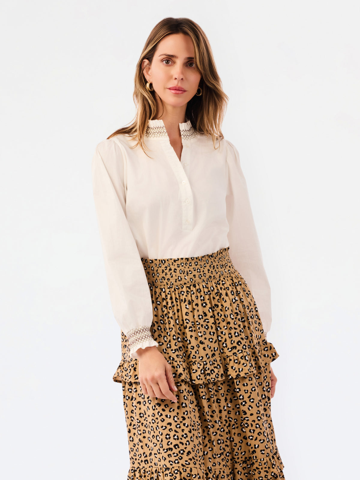 A woman modeling a white long-sleeve blouse with a lace-trimmed collar and cuffs, paired with a brown leopard-print tiered skirt, against a plain white background.