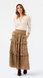 A woman modeling a long tiered skirt with a brown and black leopard print, paired with a cream-colored long-sleeve top and dark brown boots, against a plain white studio background.