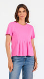 A woman modeling a bright pink short-sleeve top with a gathered peplum hem, paired with blue jeans, against a plain white studio background.