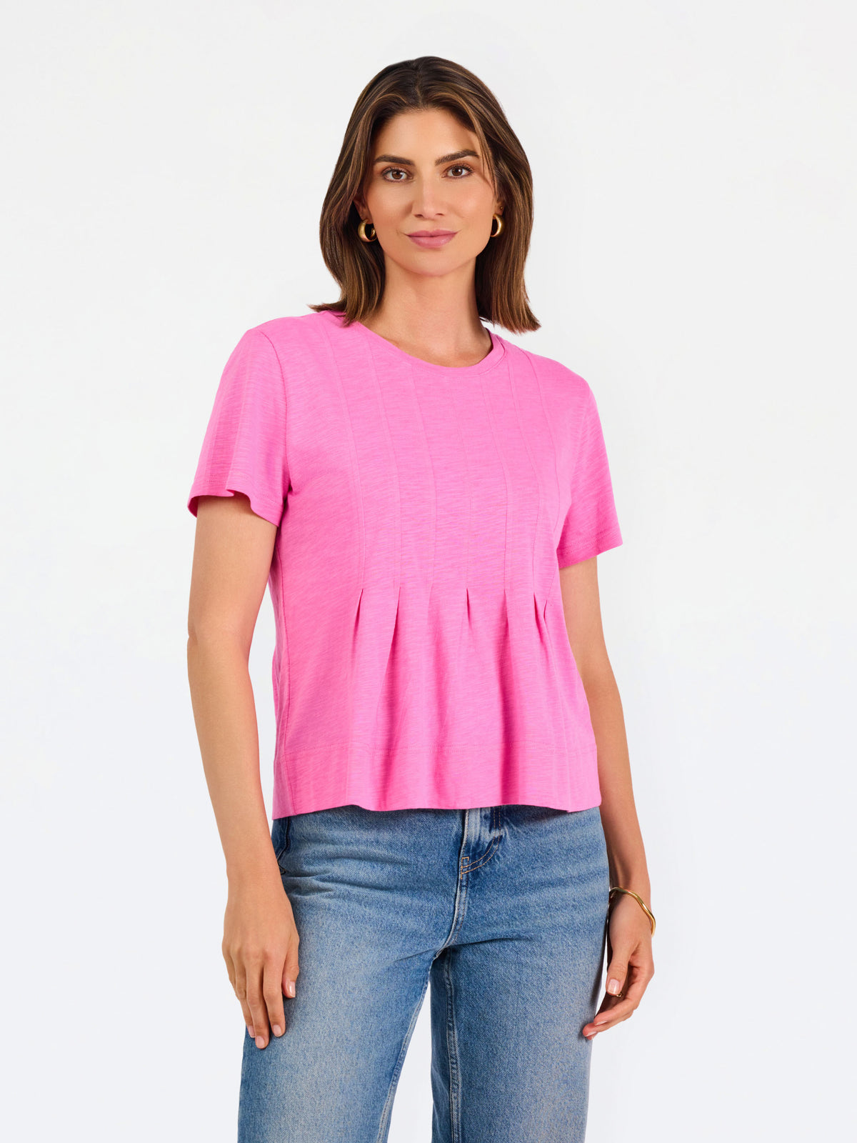 A woman modeling a bright pink short-sleeve top with a gathered peplum hem, paired with blue jeans, against a plain white studio background.