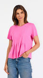 A woman modeling a bright pink short-sleeve top with a gathered peplum hem, paired with blue jeans, against a plain white studio background.