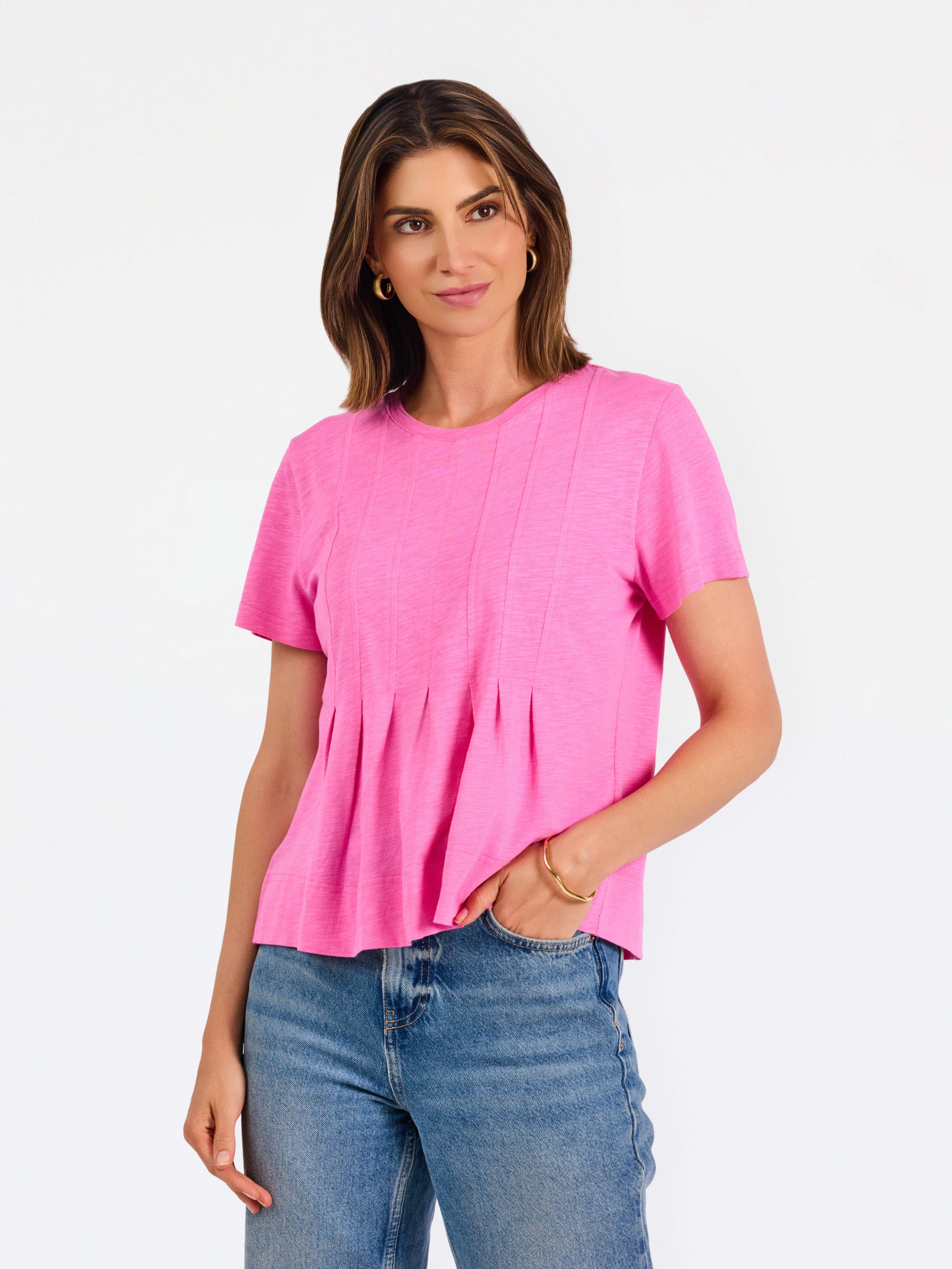 A woman modeling a bright pink short-sleeve top with a gathered peplum hem, paired with blue jeans, against a plain white studio background.