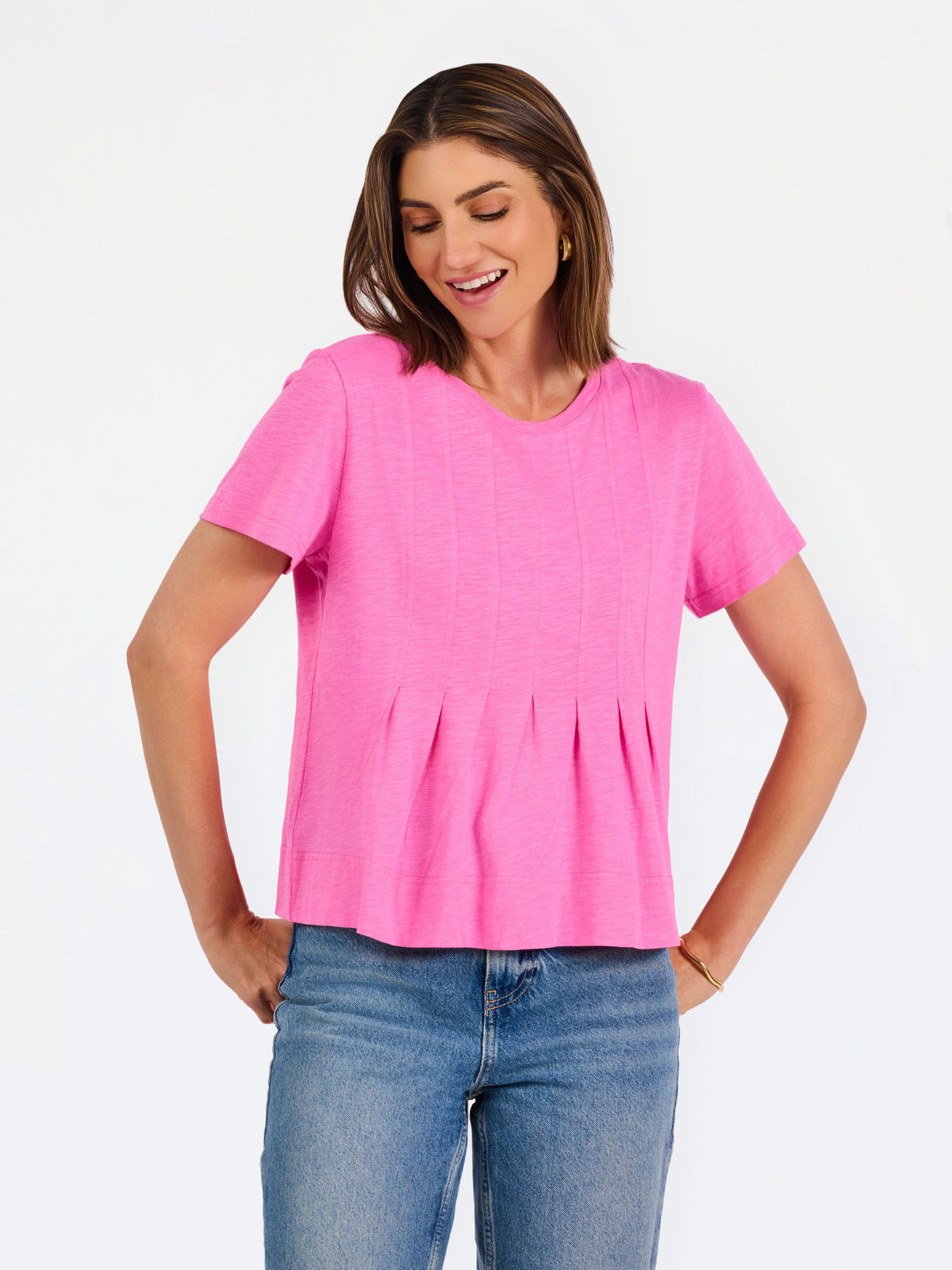 A woman modeling a bright pink short-sleeve top with a gathered peplum hem, paired with blue jeans, against a plain white studio background.