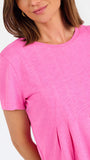 A woman modeling a bright pink short-sleeve top with a gathered peplum hem, paired with blue jeans, against a plain white studio background.