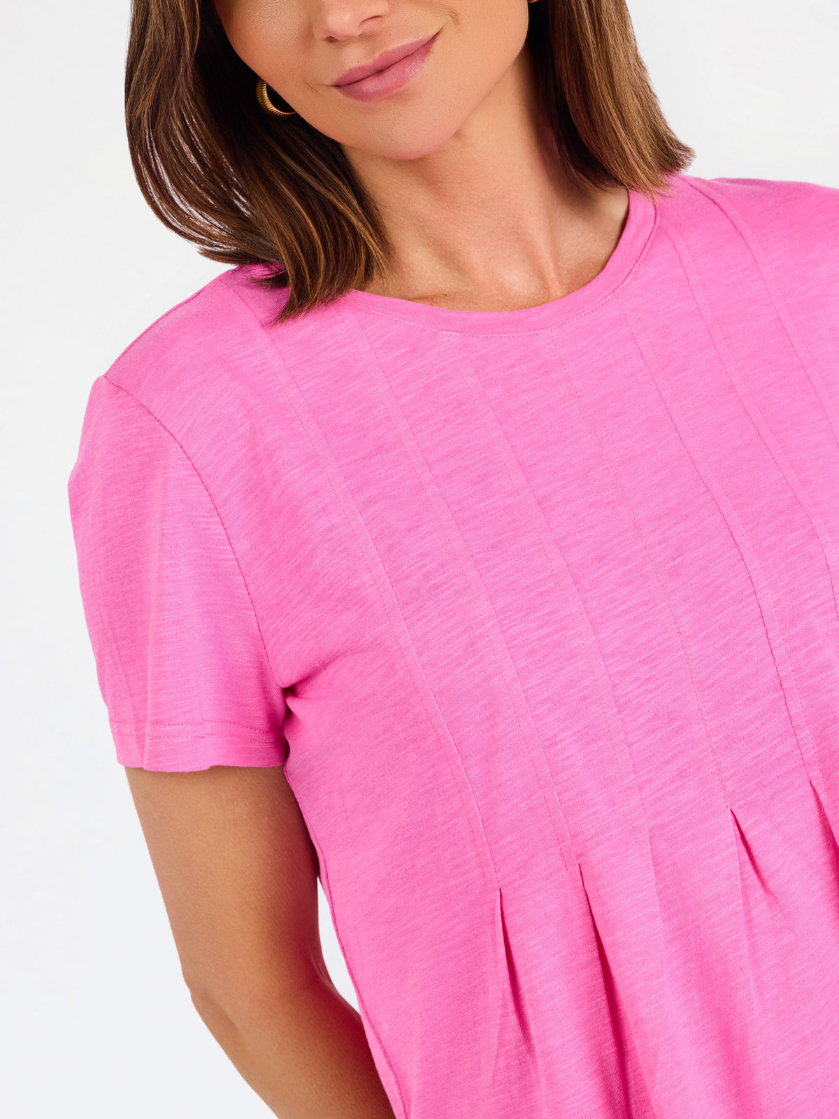 A woman modeling a bright pink short-sleeve top with a gathered peplum hem, paired with blue jeans, against a plain white studio background.