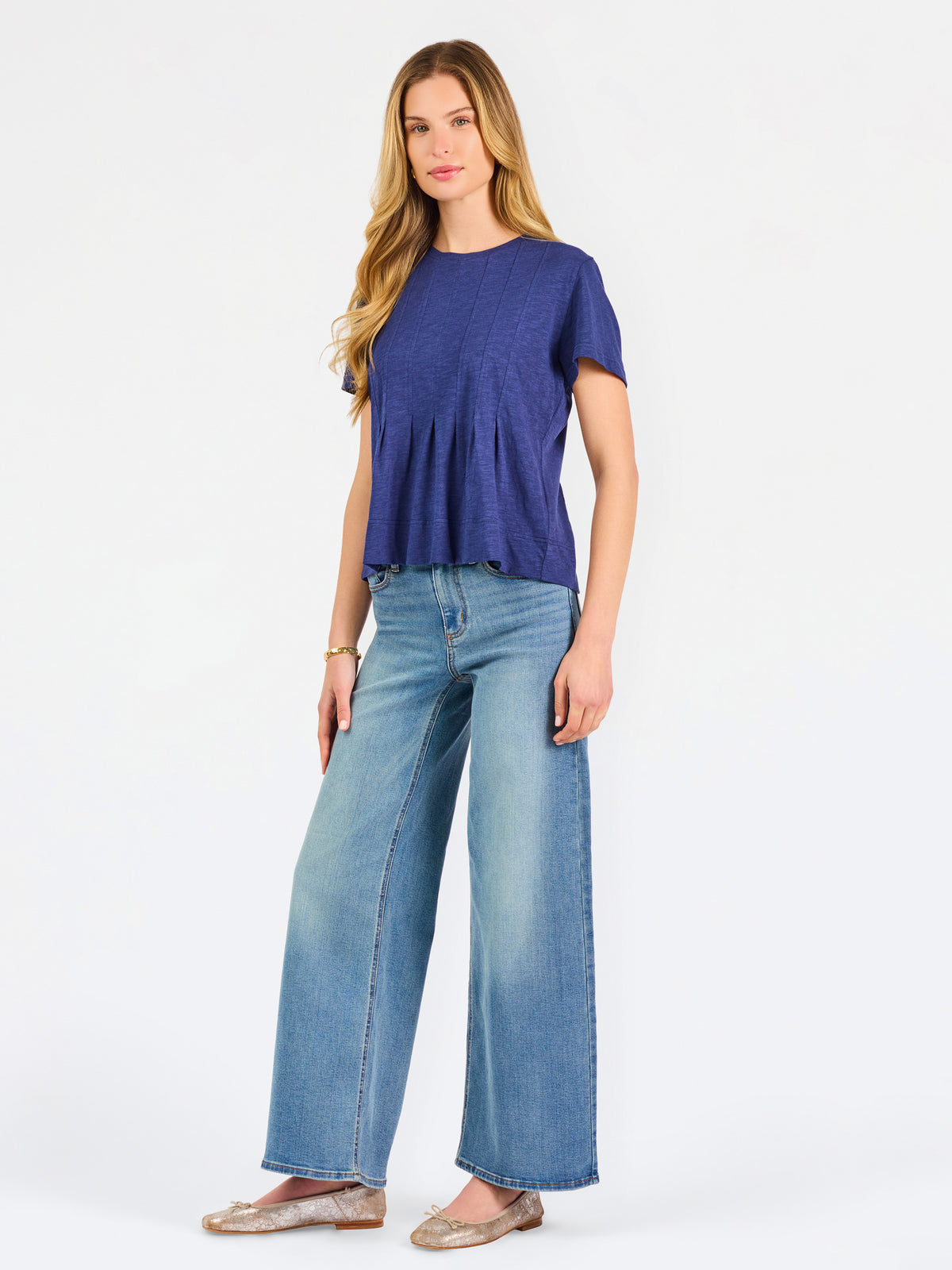 A woman modeling a short-sleeve peplum top in a heathered periwinkle blue color, paired with light-wash blue jeans, against a plain white studio background.