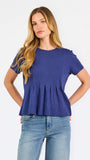 A woman modeling a short-sleeve peplum top in a heathered periwinkle blue color, paired with light-wash blue jeans, against a plain white studio background.