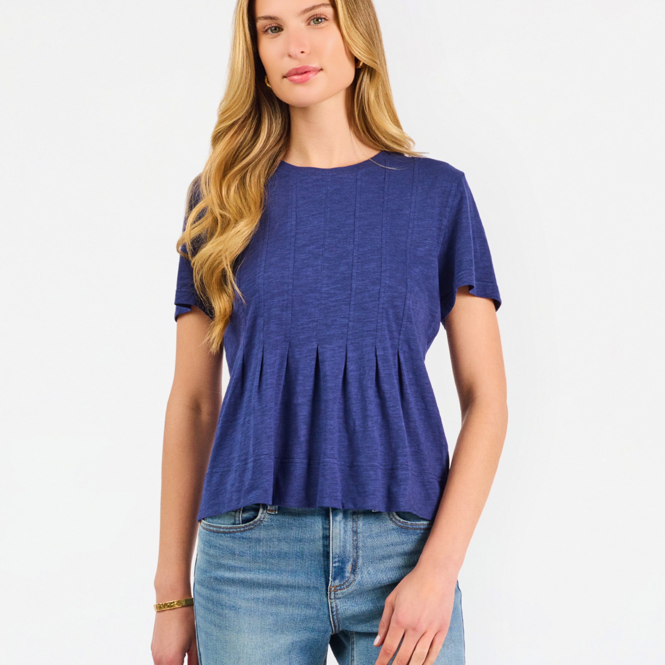 A woman modeling a short-sleeve peplum top in a heathered periwinkle blue color, paired with light-wash blue jeans, against a plain white studio background.